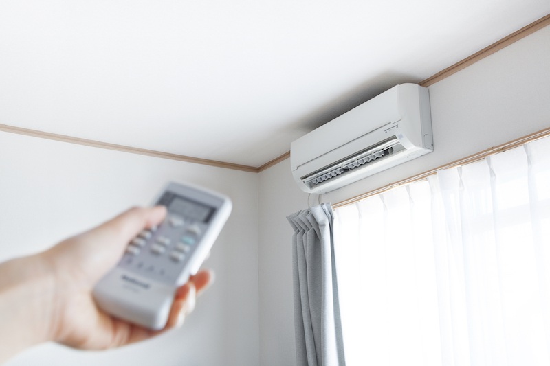 A hand pointing a remote at a Ductless Mini-Split AC System. Air Today Heating & Cooling offers Greenville Mini-Split Installation Services, including Ductless Mini-Split Air Conditioners and Mini-Split Furnaces.